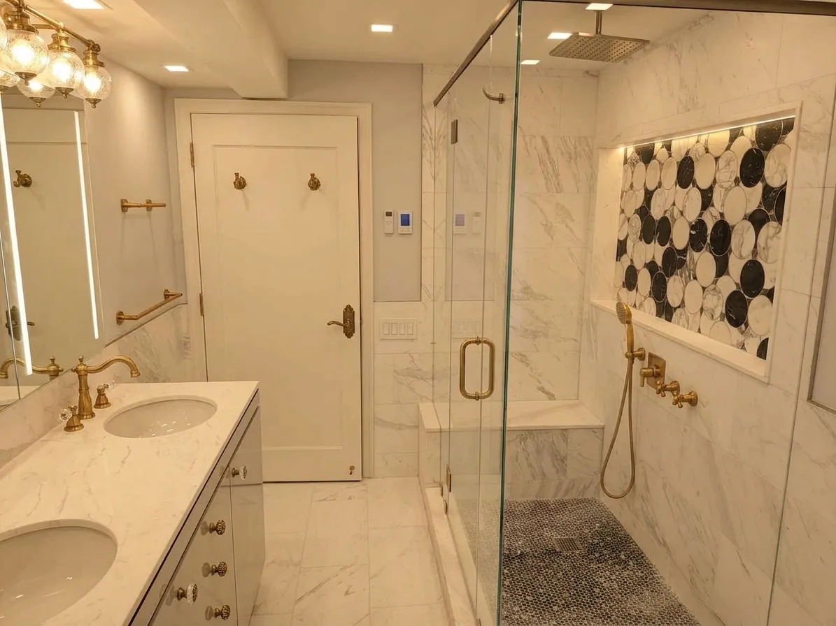 A marble shower with brass fixtures and a black-and-white penny-mosaic niche