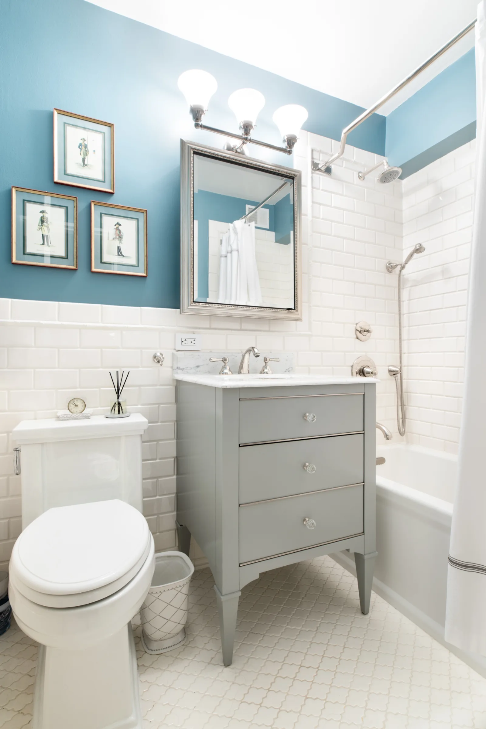 A renovated NYC bathroom with white beveled subway tile, a gray vanity, and polished nickel fixtures