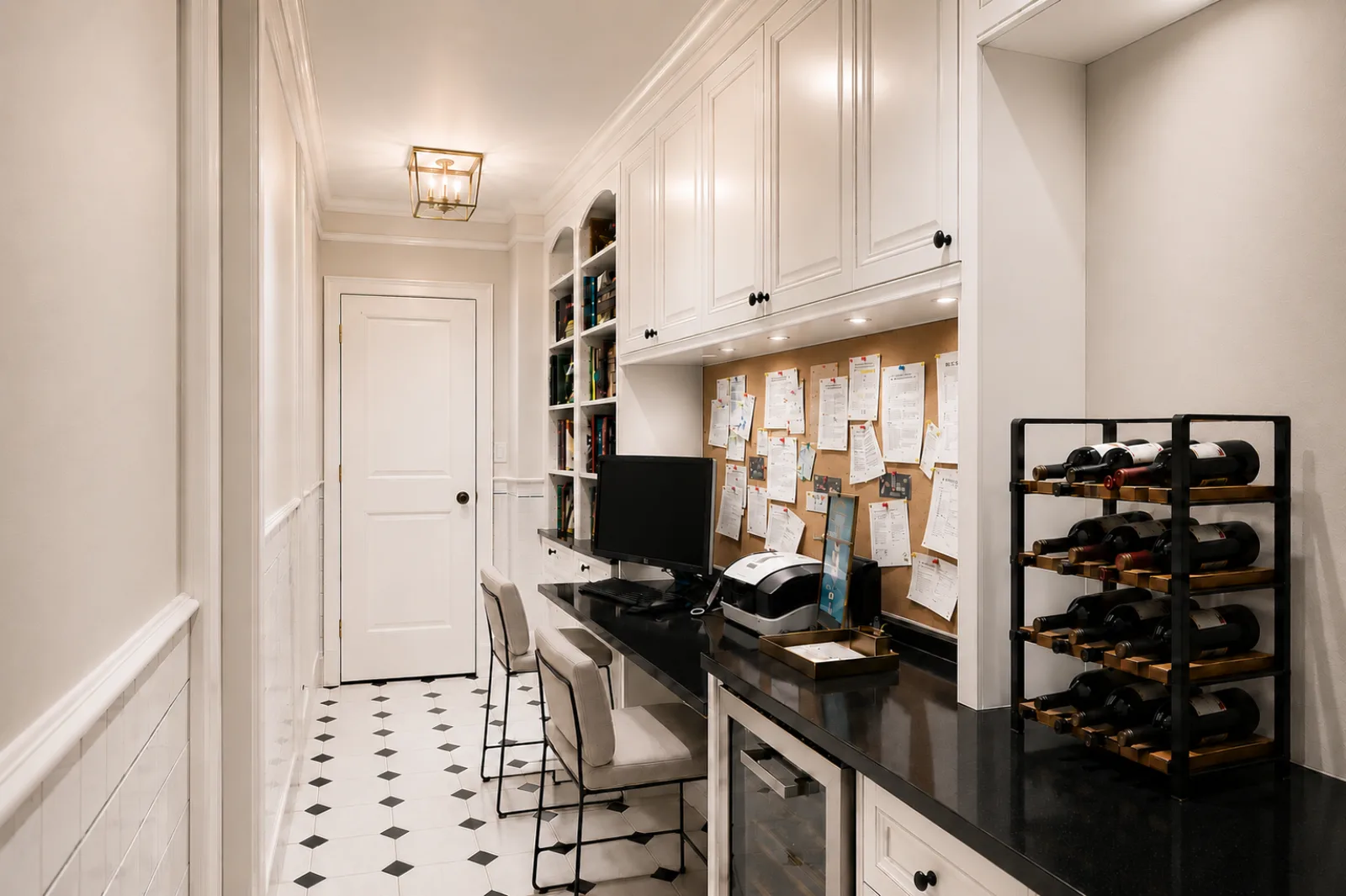 A built-in home office nook with a black stone work surface, white cabinetry, bookshelves, and a pinboard wall in a renovated NYC apartment
