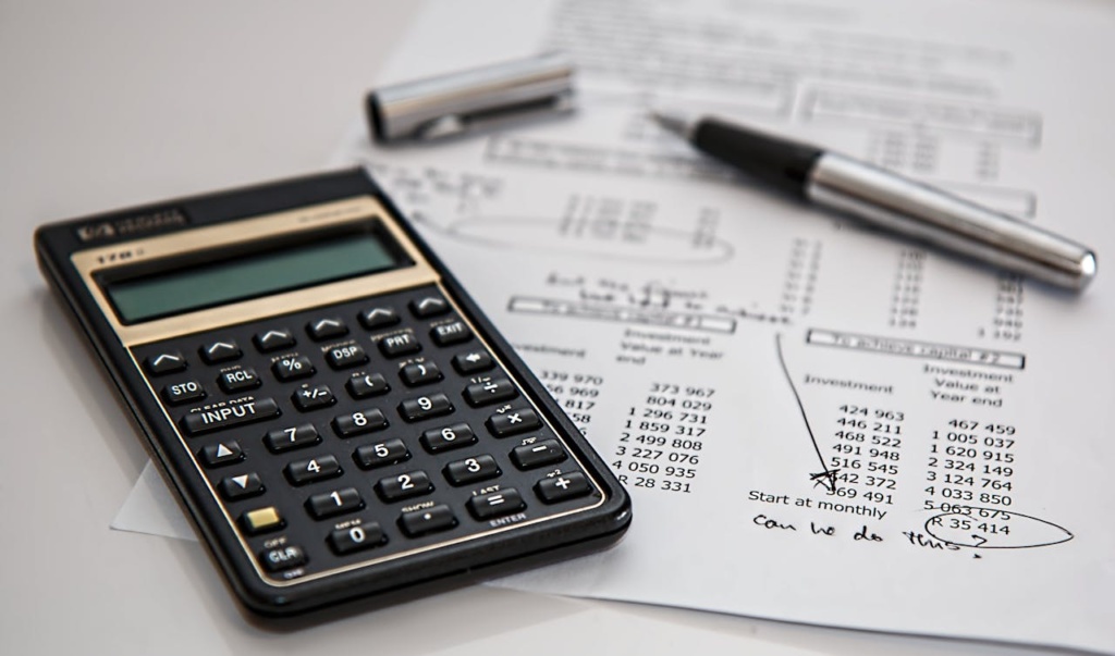 Black calculator on a piece of white paper and a silver pen.